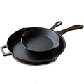 A set of two black cast iron skillets, one larger than the other, stacked inside each other on a white background.