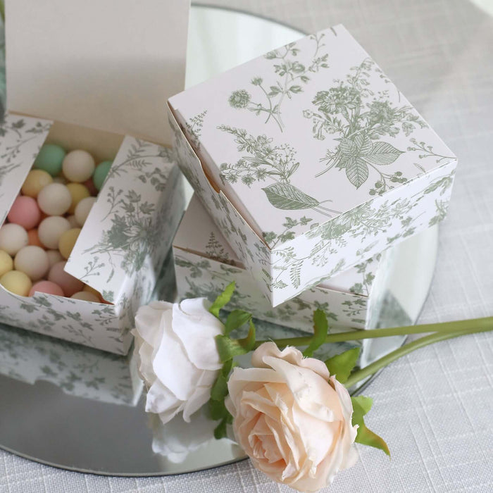 Decorative floral gift boxes with pastel candies and a rose on a reflective surface.