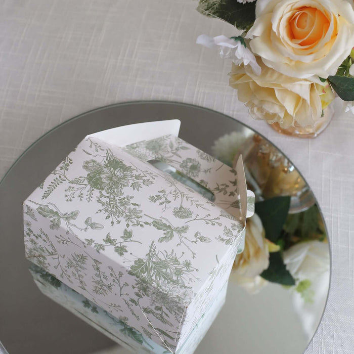 Decorative floral gift box on a reflective surface with flowers in the background.