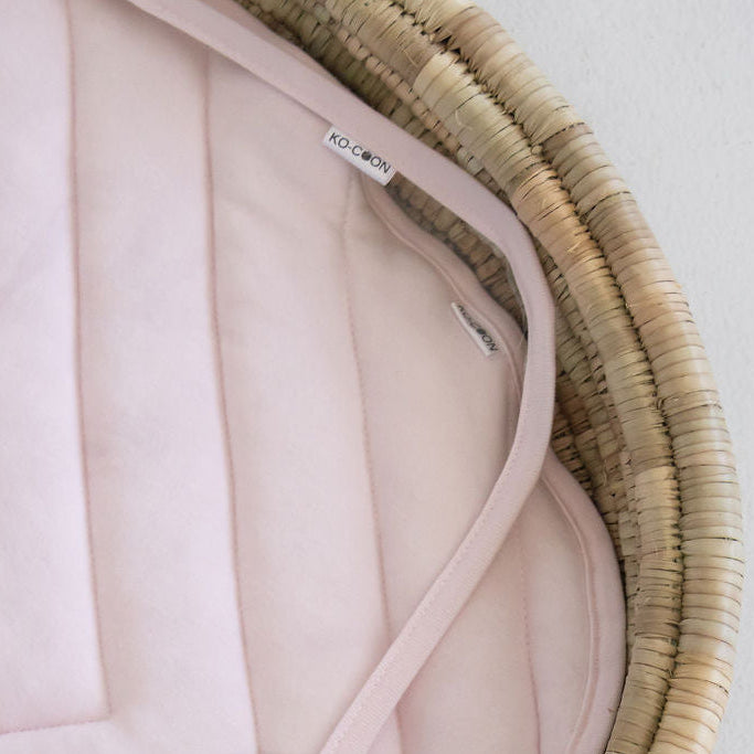 Pink quilted cover inside a wicker basket on a light gray background