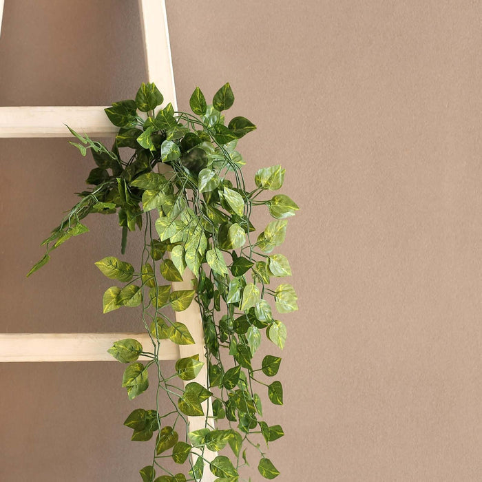 Artificial ivy garland cascading from a wooden ladder against a neutral wall.