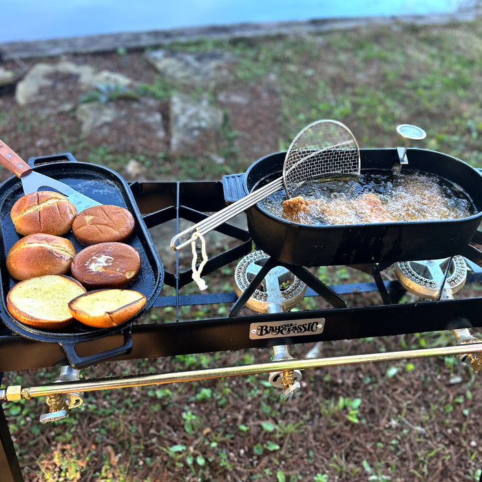 Cast Iron Oval Fryer frying chicken with a skimmer and griddle lid toasting buns outside on a cooker