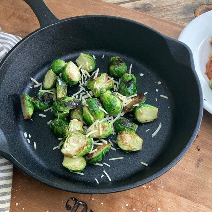 Brussel sprouts with cheese in a black cast iron skillet on a wooden table.