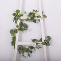 Artificial eucalyptus and rose garland on a white ladder.