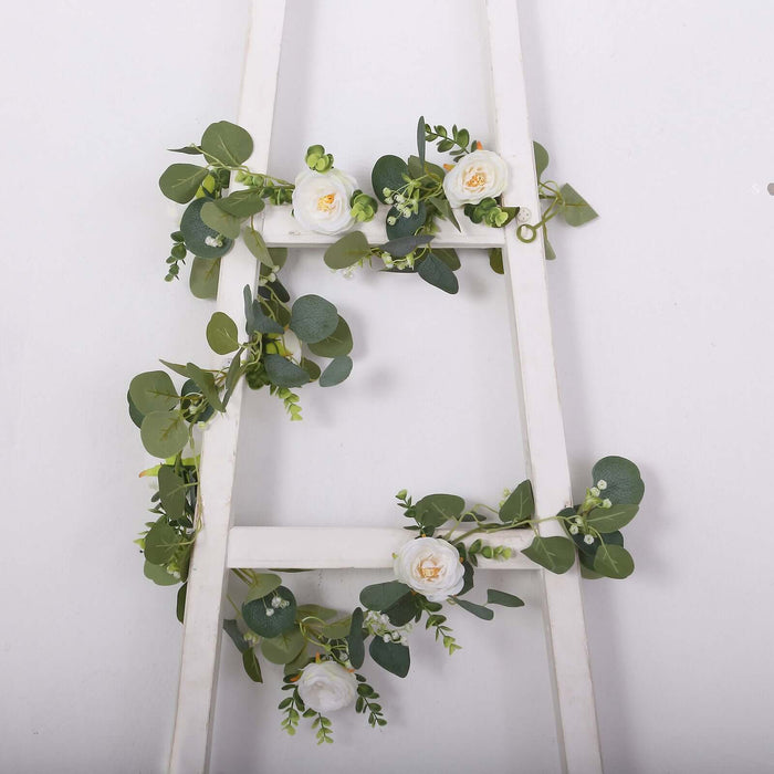 Artificial eucalyptus and rose garland on a white ladder.