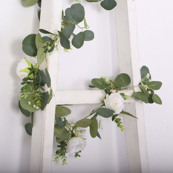 Artificial white rose and eucalyptus greenery on a wooden ladder decoration.