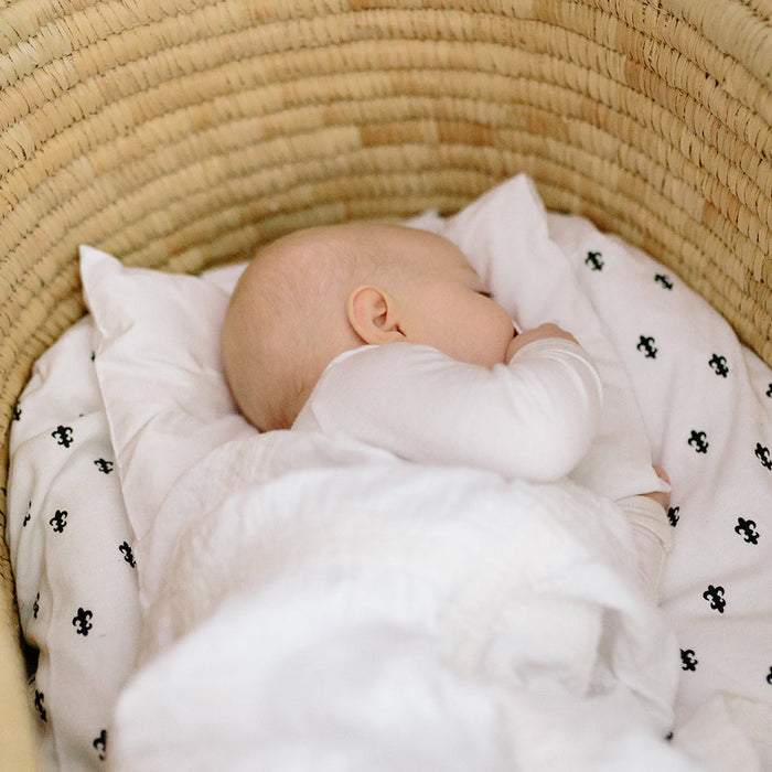 A baby lying on a merino wool baby pillow with a white pillowcase, inside a natural moses basket.