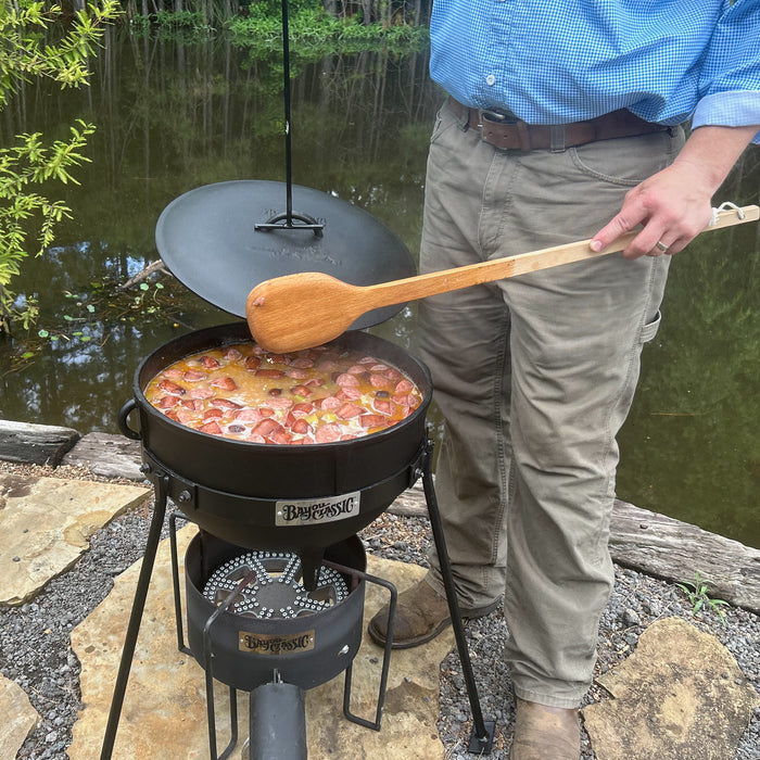 Person cooking outdoors using a cast iron jambalaya kettle and stand over an outdoor cooker
