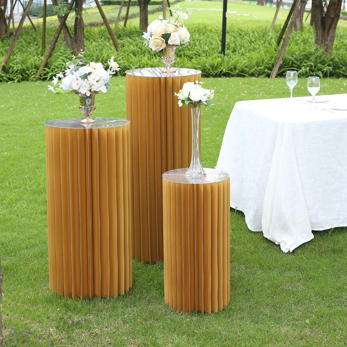 Gold pleated display pedestals with floral arrangements at an outdoor event.