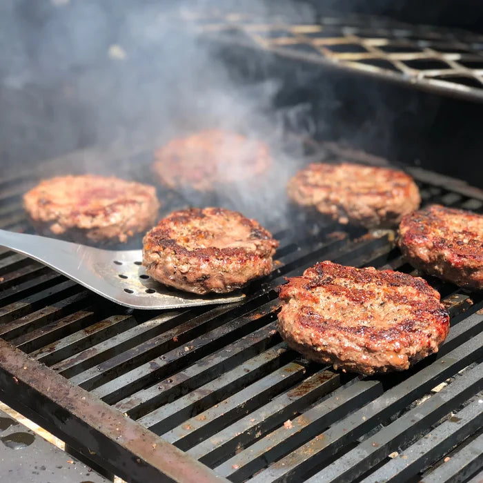 Spatula flipping hamburgers cooking on a grill with smoke