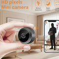 Small black camera held in a hand with smartphone showing recording app interface.