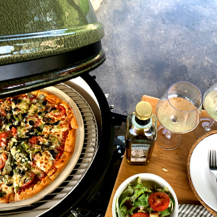 ceramic grill open with grilled pizza and ingredients sitting on a wood side shelf