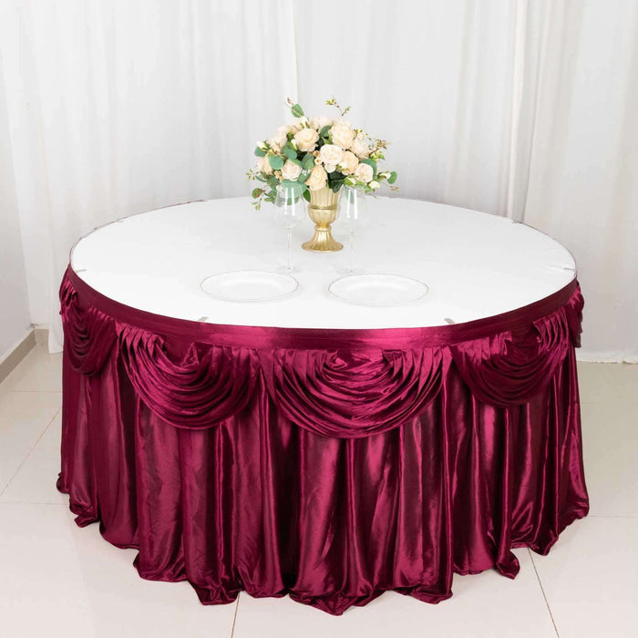 Round table with burgundy satin tablecloth and floral centerpiece.
