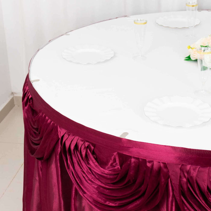 Round table draped in burgundy satin with white plates set for dining.