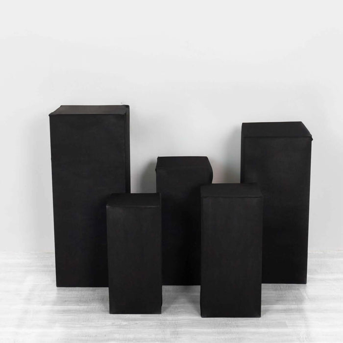 Black geometric display pedestals in various heights on a plain background.