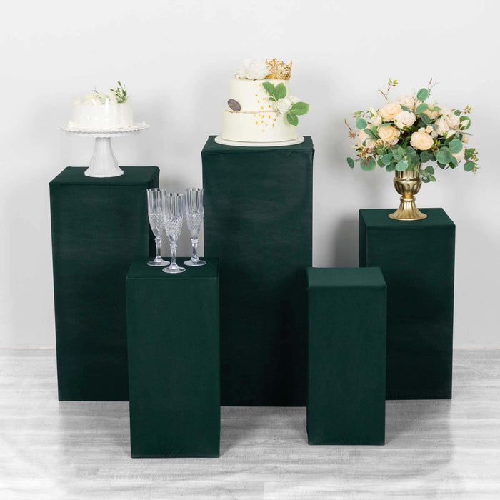 Decorative display with cakes, flowers, and glasses on green pedestals.